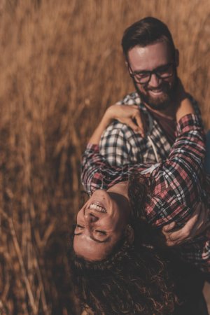 Téléchargez les photos : Couple amoureux s'amusant à l'extérieur, homme portant une femme dans ses bras, tournant ensemble et riant - en image libre de droit