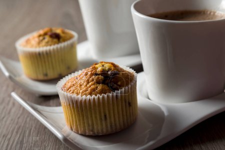 Photo for Two cups of coffee on plates next to a chocolate crunches muffins on a wooden table - Royalty Free Image