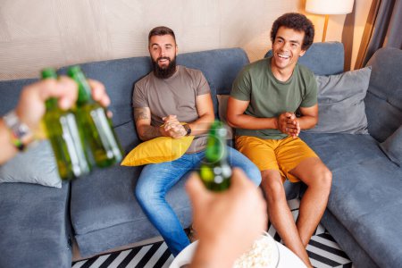 Téléchargez les photos : Vue en angle élevé du groupe d'hommes s'amusant passer du temps libre ensemble à la maison, regarder la télévision, manger du maïs soufflé et boire de la bière - en image libre de droit