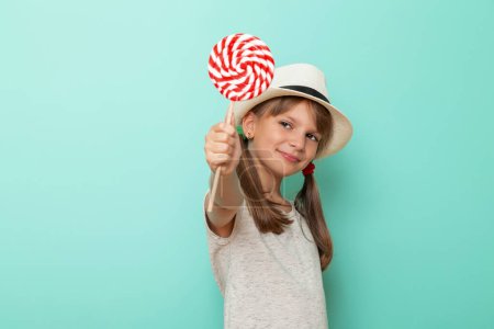 Foto de Retrato de una hermosa niña con sombrero de verano y la celebración de piruleta de colores aislados sobre fondo de color menta - Imagen libre de derechos