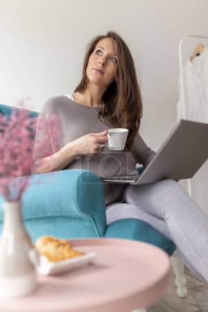 Foto de Hermosa mujer embarazada sentada en un sillón, usando una computadora portátil y tomando café - Imagen libre de derechos