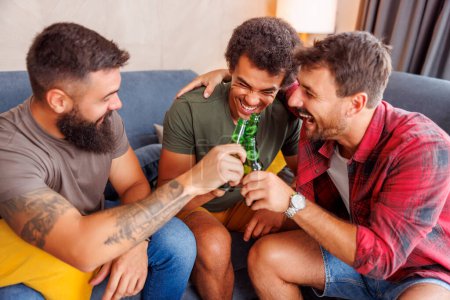 Foto de Grupo de amigos varones que se divierten pasando tiempo libre juntos en casa, haciendo un brindis y bebiendo cerveza - Imagen libre de derechos