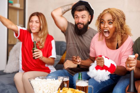 Foto de Grupo de jóvenes amigos alegres divirtiéndose viendo fútbol en la televisión, animando después de que su equipo anotara un gol - Imagen libre de derechos