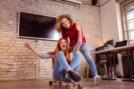 Téléchargez les photos : Des collègues d'affaires qui s'amusent à skater au bureau pendant une pause ; des gens d'affaires qui s'amusent dans un espace de coworking, faisant du skateboard - en image libre de droit