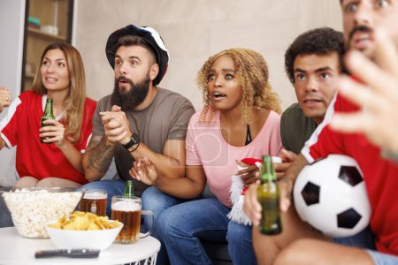 Téléchargez les photos : Groupe d'amis regarder match de championnat du monde de football à la télévision à la maison, acclamations, manger du maïs soufflé et boire de la bière - en image libre de droit