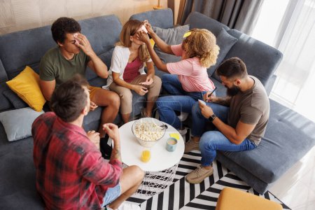 Photo for High angle view of group of cheerful friends having fun spending leisure time together at home gathering, playing word guessing game, writing words on sticky notes - Royalty Free Image