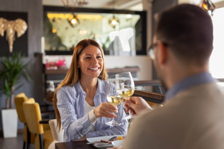 Téléchargez les photos : Jeune couple amoureux à un rendez-vous, assis à une table de restaurant, lever des verres de vin et porter un toast tout en déjeunant - en image libre de droit