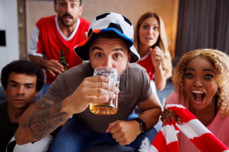 Foto de Grupo de alegres fanáticos del fútbol divirtiéndose bebiendo cerveza y viendo el juego del campeonato mundial en la televisión en casa - Imagen libre de derechos