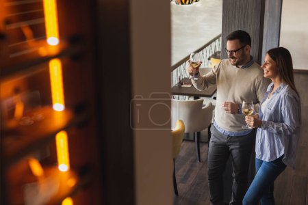 Photo for Young couple in love on a date in a restaurant, raising glasses of wine and making a toast while waiting for a table - Royalty Free Image
