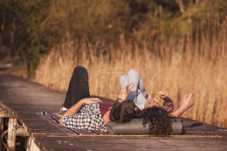 Téléchargez les photos : Couple amoureux couché sur une couverture de pique-nique sur les quais du lac, s'amuser tout en faisant des bulles de savon et profiter d'une belle journée d'automne ensoleillée dans la nature - en image libre de droit
