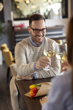 Téléchargez les photos : Jeune couple amoureux à un rendez-vous, assis à une table de restaurant, lever des verres de vin et porter un toast tout en célébrant l'anniversaire - en image libre de droit