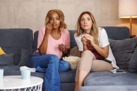 Foto de Dos amigas divirtiéndose pasando tiempo libre juntas en casa, viendo películas de miedo en la televisión y comiendo palomitas de maíz - Imagen libre de derechos