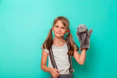 Téléchargez les photos : Portrait d'une belle petite fille jouant avec une marionnette hippopotame isolée sur fond couleur menthe - en image libre de droit