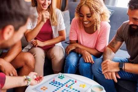 Foto de Grupo de jóvenes amigos alegres que se divierten jugando juego de mesa ludo mientras pasan tiempo juntos en casa - Imagen libre de derechos