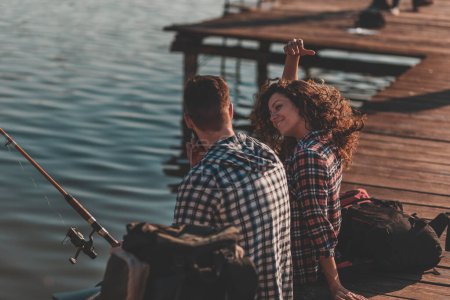 Téléchargez les photos : Couple amoureux assis sur les quais du lac, pêchant et profitant d'une belle journée ensoleillée d'automne dans la nature - en image libre de droit