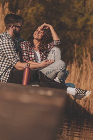 Photo for Young couple in love sitting at lake docks, enjoying a beautiful sunny autumn day in nature - Royalty Free Image