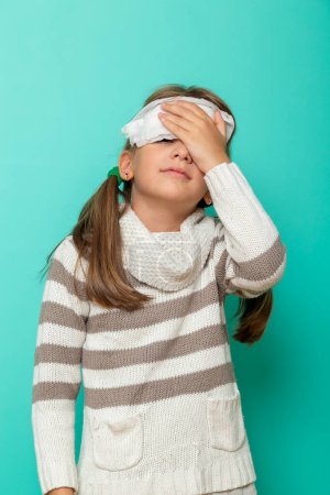 Foto de Retrato de una niña pequeña con fiebre, sosteniendo una compresa fría en la frente, tratando de bajar la fiebre - Imagen libre de derechos