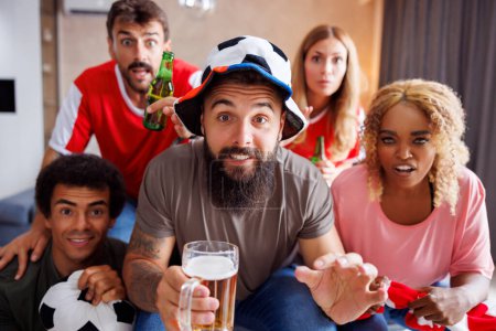 Téléchargez les photos : Groupe d'amis joyeux fans de football s'amuser à encourager, boire de la bière et regarder le match du championnat du monde à la télévision à la maison - en image libre de droit