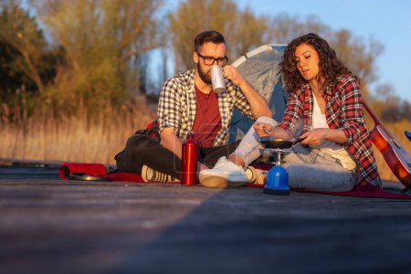 Téléchargez les photos : Couple amoureux d'une aventure de camping en plein air, faire le dîner sur les quais d'un lac et profiter d'une belle journée dans la nature - en image libre de droit