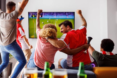 Téléchargez les photos : Groupe de jeunes amis s'amuser à regarder le match de football à la télévision, boire de la bière et encourager ; fans de football regarder le match à la maison célébrer après que leur équipe marquer un but - en image libre de droit