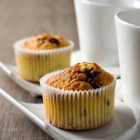 Photo for Two cups of coffee on plates next to a chocolate crunches muffins on a wooden table - Royalty Free Image