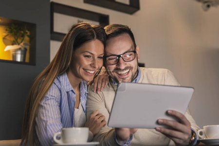 Téléchargez les photos : Beau jeune couple assis à une table de restaurant, buvant du café et ayant un appel vidéo à l'aide d'un ordinateur tablette - en image libre de droit