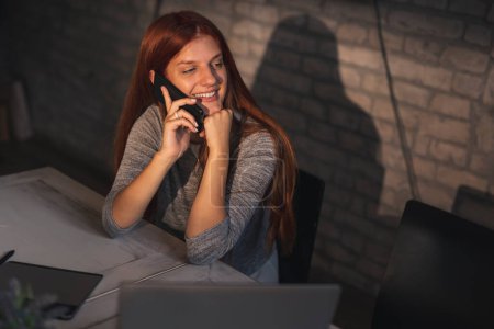 Téléchargez les photos : Femme travaillant à distance de la maison, parlant au téléphone tout en travaillant sur un ordinateur portable - en image libre de droit