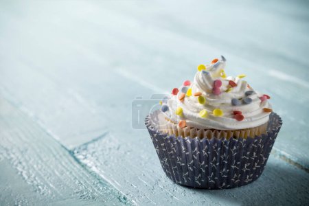 One nicely decorated muffin, with cream and colorful sprinkles placed on light blue wooden boards background