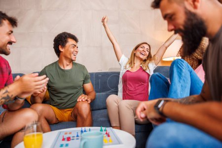 Photo for Group of cheerful young friends having fun playing ludo board game while spending time together at home - Royalty Free Image