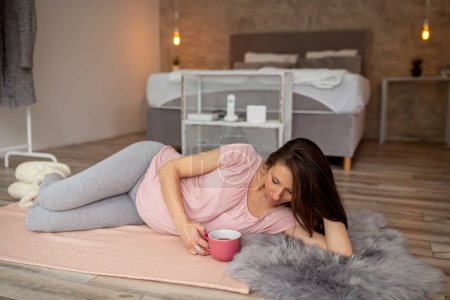 Téléchargez les photos : Belle femme enceinte se détendre à la maison, boire une tasse de thé chaud et profiter de son temps libre - en image libre de droit