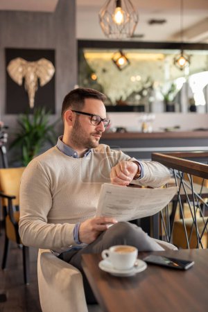 Téléchargez les photos : Homme assis à la table du restaurant, regardant sa montre, vérifiant l'heure en attendant quelqu'un qui est en retard - en image libre de droit