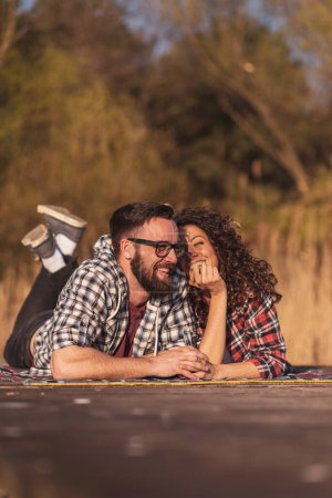 Téléchargez les photos : Couple s'amuser sur un lac quais pique-nique, couché sur une couverture de pique-nique et profiter d'une belle journée d'automne dans la nature - en image libre de droit