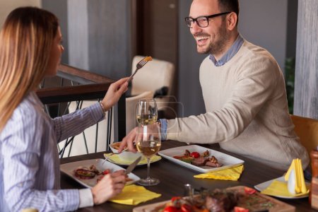 Téléchargez les photos : Beau jeune couple amoureux déjeunant au restaurant, dégustant la nourriture de l'autre et s'amusant - en image libre de droit