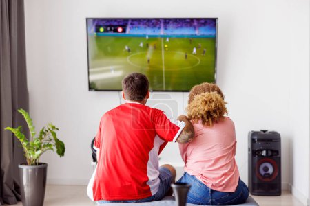 Téléchargez les photos : Couple s'amuser à regarder le match de championnat du monde de football à la télévision à la maison, acclamant pour leur équipe nationale - en image libre de droit