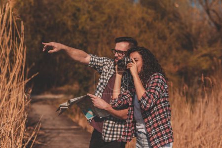 Photo for Couple of tourists reading a map in search for a hiking trail, having fun on summertime adventure trip and taking photos - Royalty Free Image