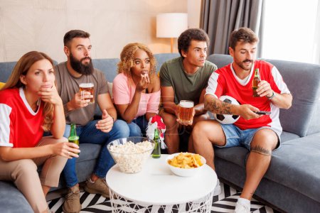 Téléchargez les photos : Groupe d'amis regarder match de championnat du monde de football à la télévision à la maison, acclamations, manger du maïs soufflé et boire de la bière - en image libre de droit