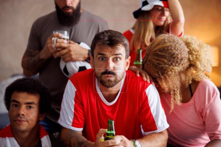 Téléchargez les photos : Groupe de fans de football regarder le match à la télévision déçu après leur équipe perdant et ratant le but - en image libre de droit