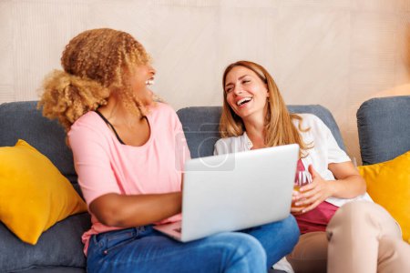 Foto de Dos mujeres que se divierten usando el ordenador portátil mientras pasan tiempo libre juntos en casa, navegar por Internet - Imagen libre de derechos