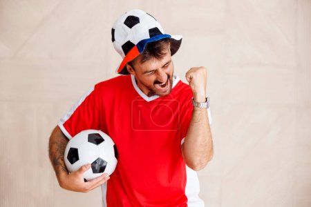 Photo for Portrait of male football fan wearing sports jersey holding cheering props celebrating his team scoring a goal at  the world championship game - Royalty Free Image