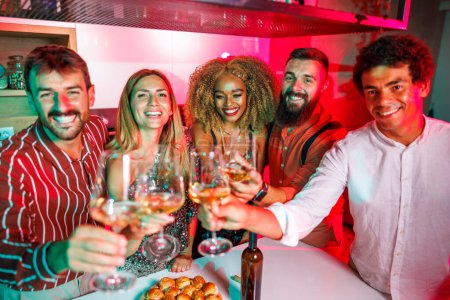 Photo for Group of cheerful young friends having fun at house party, making a toast raising glasses of wine towards the camera, dancing and drinking - Royalty Free Image