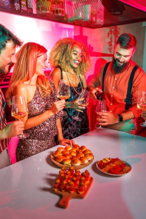 Téléchargez les photos : Groupe d'amis joyeux s'amuser à une fête, l'ouverture d'une bouteille de vin tout en célébrant les amis anniversaire ensemble à la maison - en image libre de droit