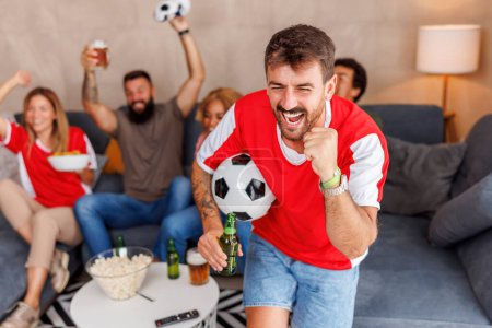 Téléchargez les photos : Groupe de fans de football joyeux s'amuser à applaudir et célébrer après que leur équipe a marqué un but tout en regardant le match du championnat du monde à la télévision à la maison - en image libre de droit