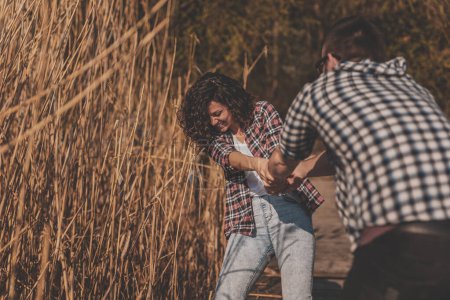 Téléchargez les photos : Couple amoureux profitant d'une belle journée ensoleillée d'automne en plein air, s'amusant tout en se tenant la main et tournant sur les quais du lac - en image libre de droit