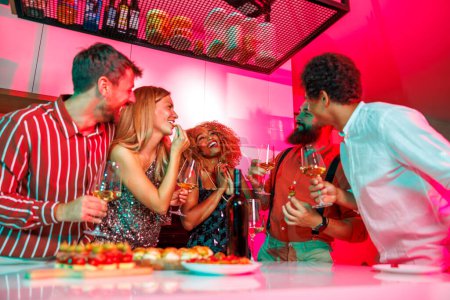 Foto de Grupo de amigos de 30 años que se divierten en la fiesta de la casa, cantando, bailando, bebiendo vino y comiendo pasteles de cóctel - Imagen libre de derechos