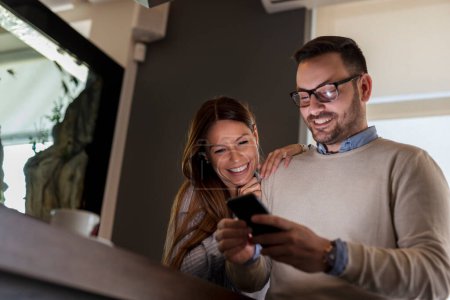 Téléchargez les photos : Beau jeune couple assis à une table de restaurant, buvant du café et utilisant un smartphone - en image libre de droit