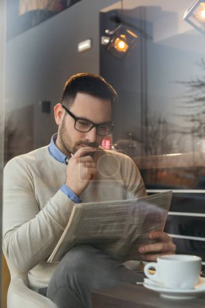 Foto de Retrato de un hombre pensativo sentado en la mesa de un restaurante, leyendo periódicos y tomando café - Imagen libre de derechos