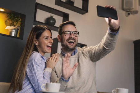 Téléchargez les photos : Jeune couple amoureux à un rendez-vous, assis à une table de restaurant, boire du café et prendre un selfie - en image libre de droit