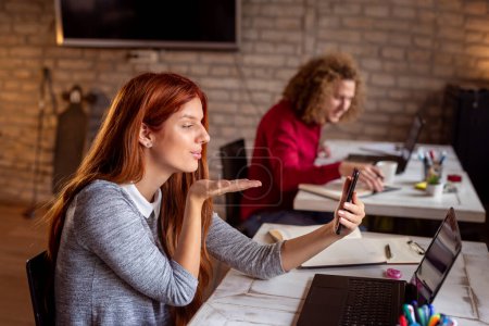 Téléchargez les photos : Jeunes en pause dans un bureau moderne ; pigistes travaillant dans un espace de coworking, femme ayant un appel vidéo à l'aide d'un téléphone intelligent - en image libre de droit