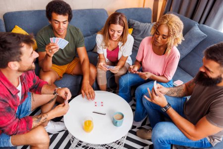 Téléchargez les photos : Joyeux jeunes amis passer du temps ensemble à la maison, avoir du plaisir à jouer à des jeux de cartes - en image libre de droit