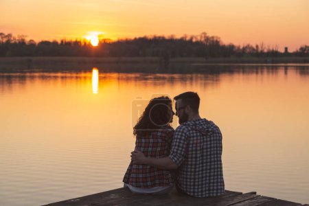 Téléchargez les photos : Jeune couple amoureux camper sur les quais du lac, embrasser, embrasser et profiter d'un magnifique coucher de soleil sur le lac - en image libre de droit